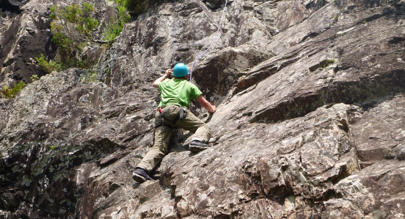 A person wearing safety gear and secured by ropes climbs up a rock wall.